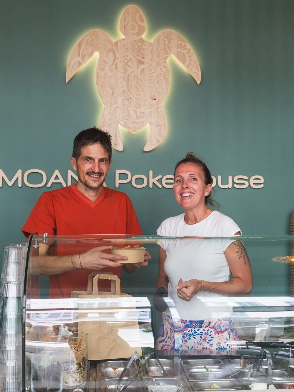 Nicolas und Marie, die Gründer von Moana Poke House, vor der leuchtenden Schildkröte
